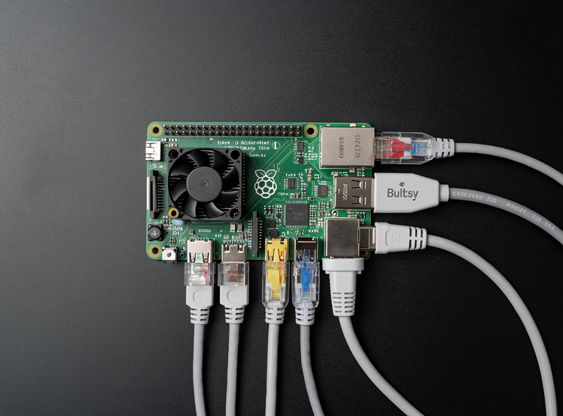 Raspberry Pi 5 in a black case with USB Ethernet adapter connected and active status lights running as a pfSense router on a homelab desk