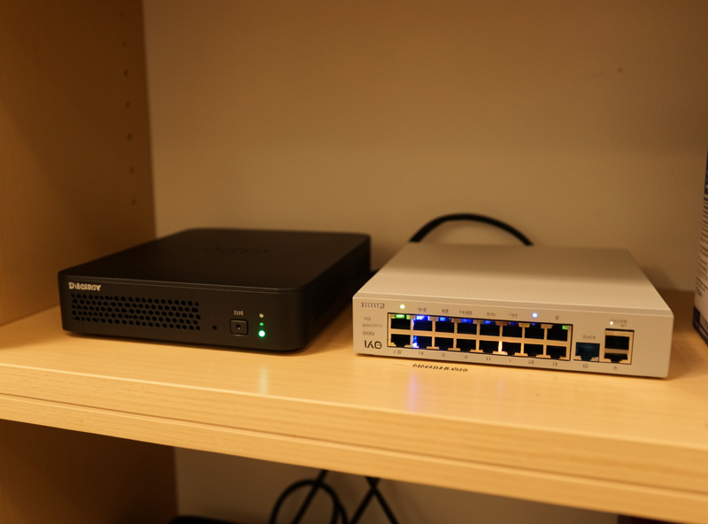 A low-power mini PC running a free hypervisor next to a managed network switch on a homelab shelf