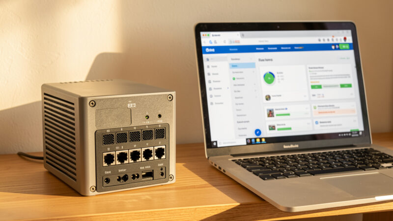 Fanless firewall appliance on a shelf beside a laptop showing the firewall web dashboard
