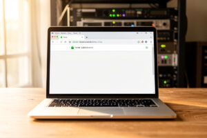 Laptop browser address bar showing a green padlock and a home subdomain with a network rack behind
