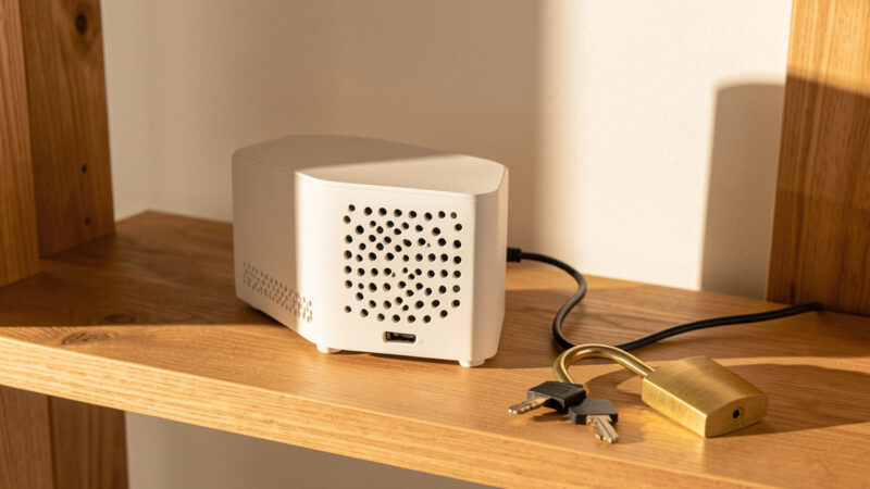 Small fanless home server on a wooden shelf with a brass padlock and key resting nearby in warm light