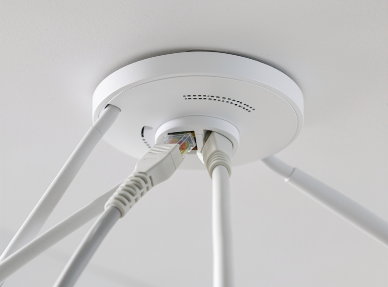 Wi-Fi 7 ceiling access point being connected to a Cat6a ethernet cable with a PoE injector